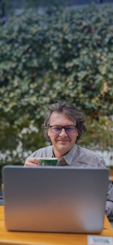 Image d’un homme souriant portant des lunettes, une tasse dans la main droite et consultant son ordinateur portable